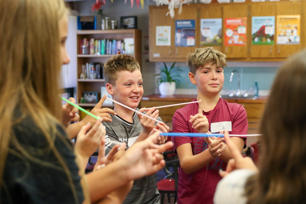two 7th grade boys smiling holding up straws with their fingers during an ice breaker game