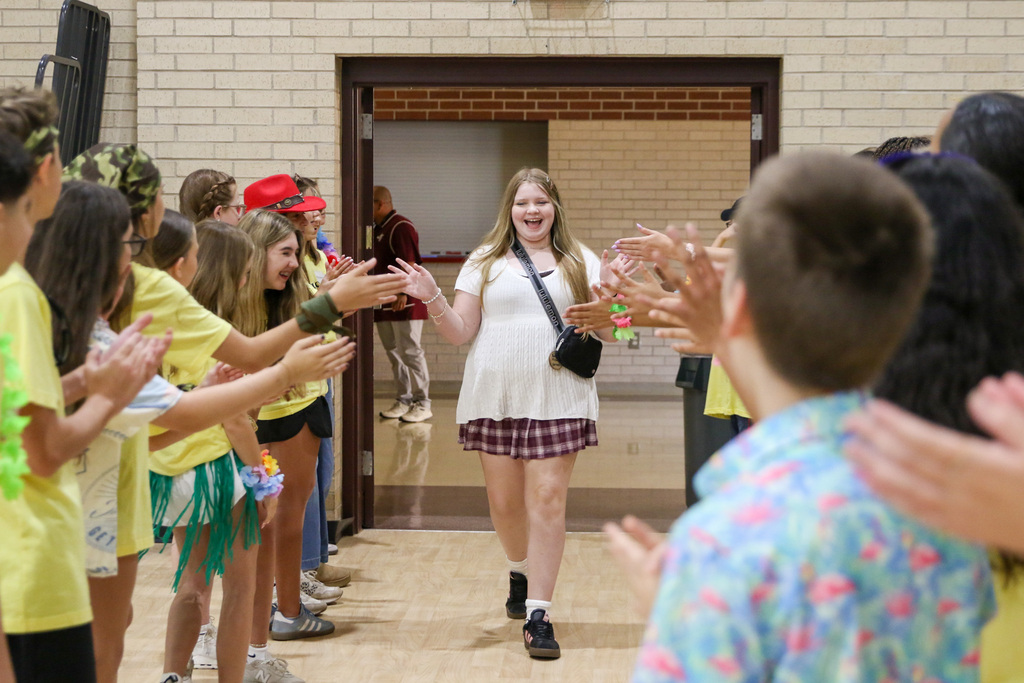 7th grade girl walking into orientation being greeted by 8th grade WEB leaders cheering for her and giving her high fives