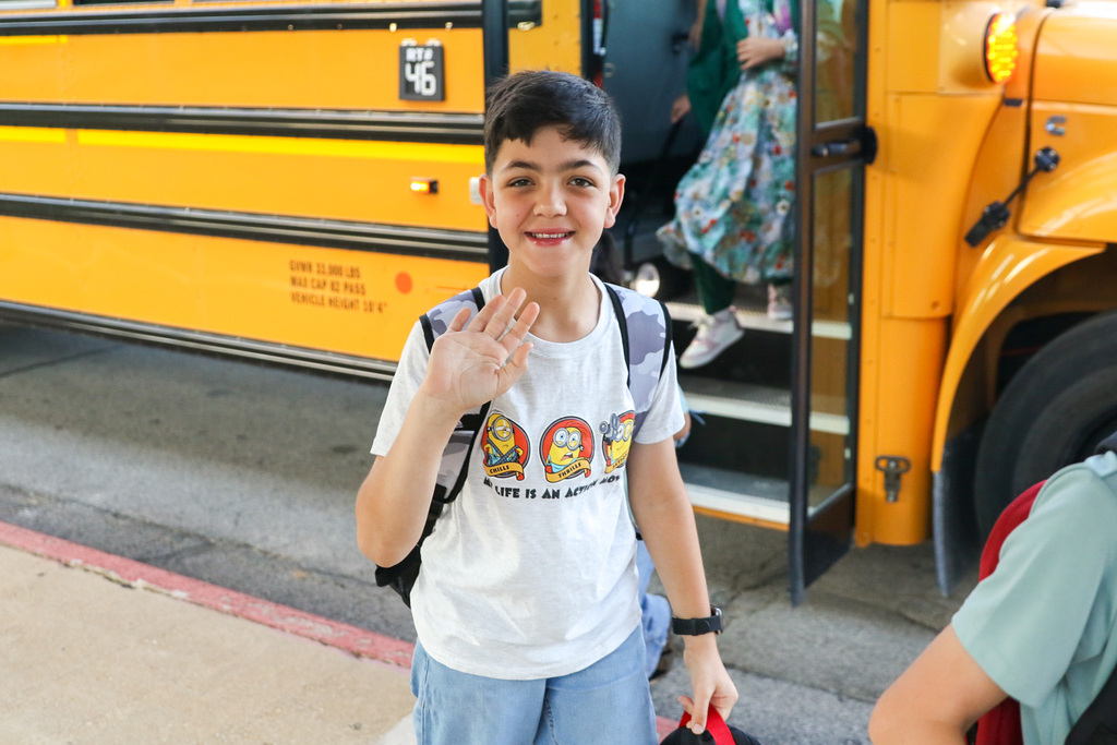 Boy who just stepped off the bus behind him stops to wave and smile for a photo