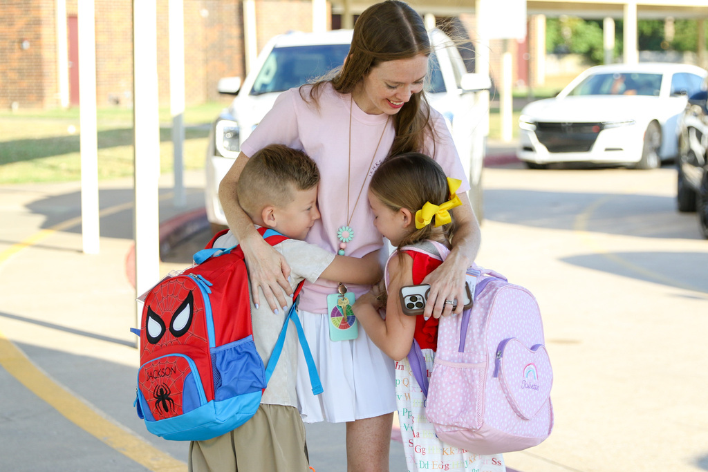 teacher giving a hug to two elementary students in the car line