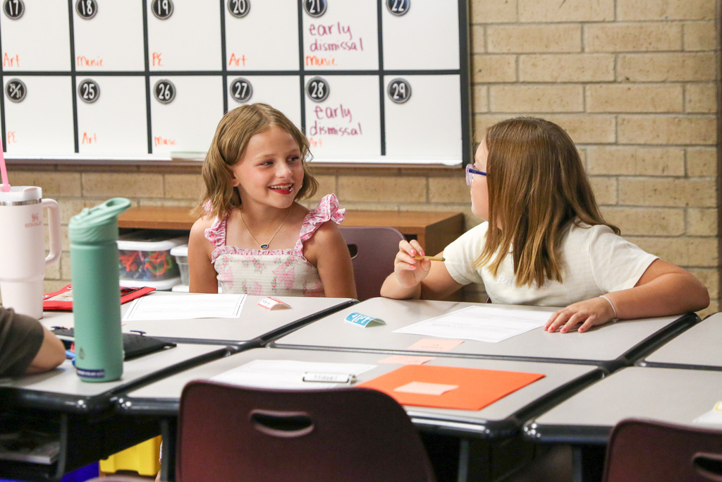 two intermediate girls sitting at their desk smiling