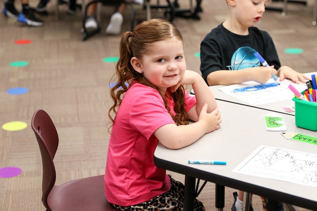 kindergarten girl sitting in her seat at her desk looking at the camera and smiling