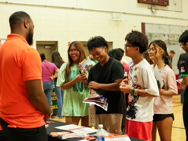 4 students smiling talking to a college representative 