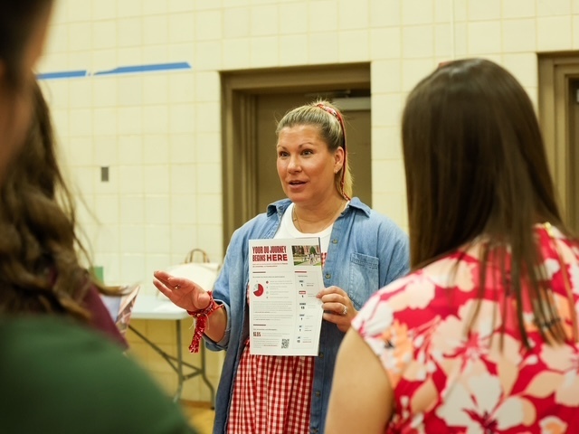 college representative standing with a fact sheet chatting to students about the university she is representing