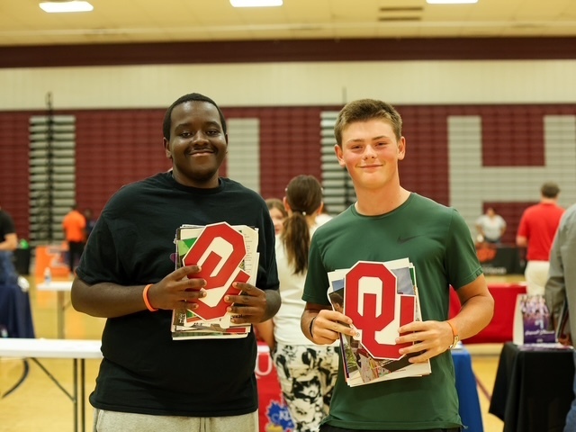 two boys holding university of oklahoma and other college brochures smiling for a photo