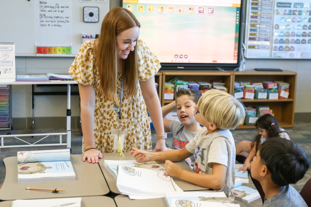 teacher at a students desk looking down at them smiling while the student is looking up at her