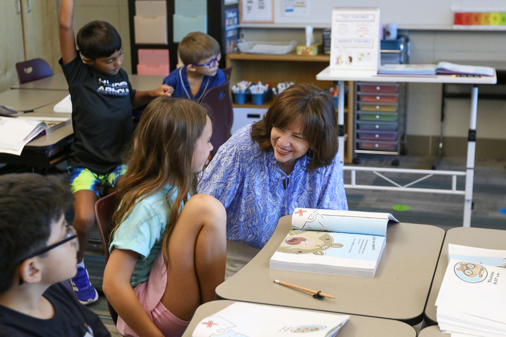 dr. butterfield down next to a students desk and is laughing with her.
