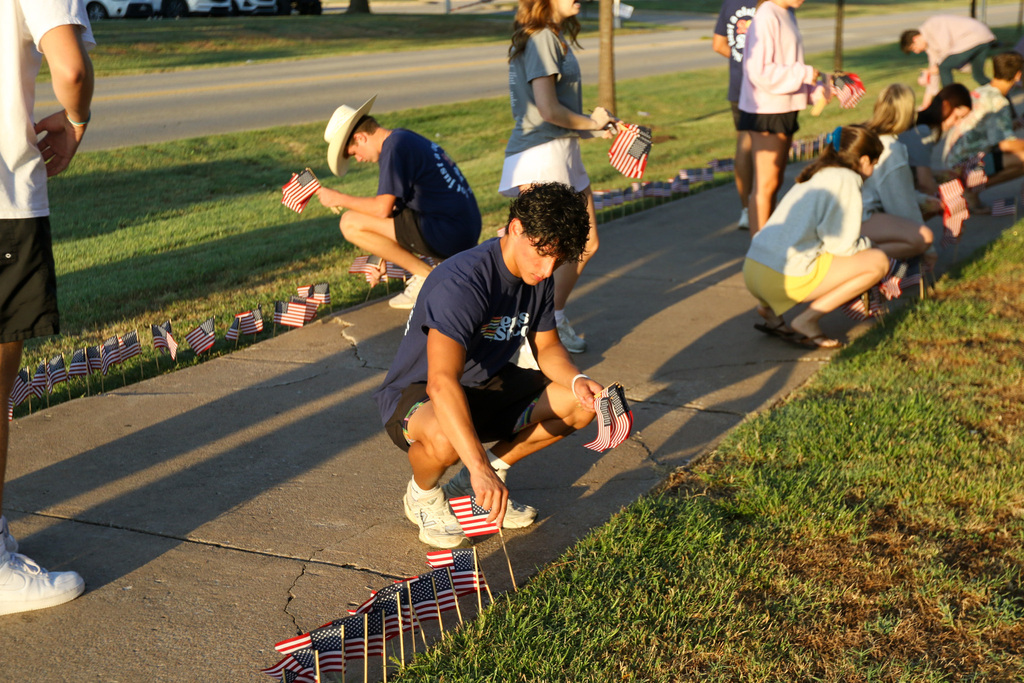 boy putting flags in the ground with other students around him in the background doing th same