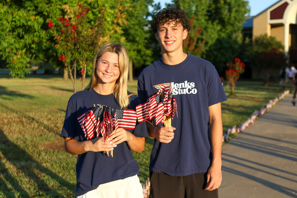 two high school students posing together for a photo. they both are holding a handful of flags