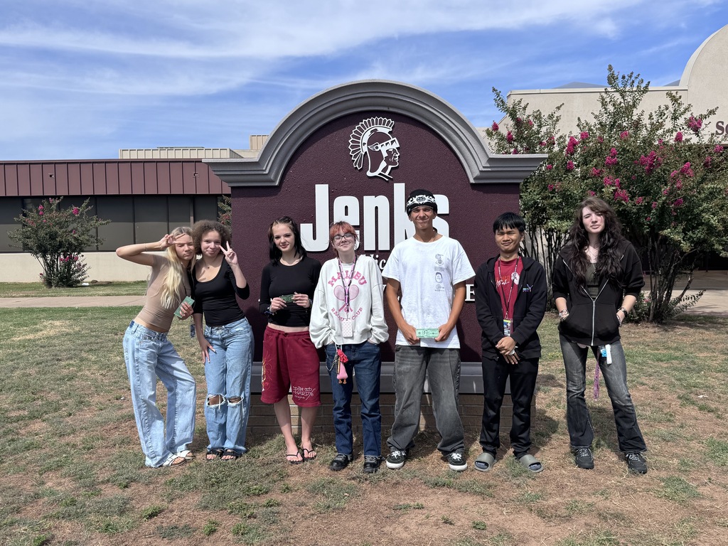 A group of 7 students in front of school sign