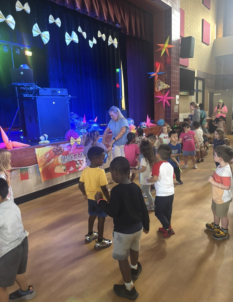 Elementary students dance around in a decorated event area.