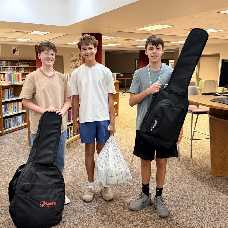 two male students with guitar cases as backpacks, and one with a pillowcase