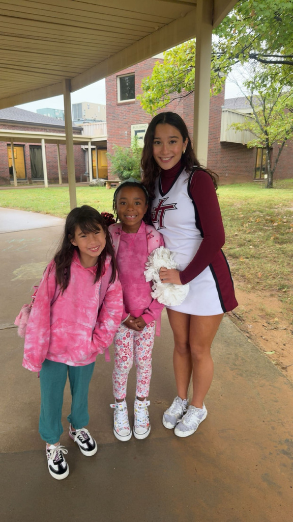 Cheerleader standing and smiling next to two girls outside of East Elementary