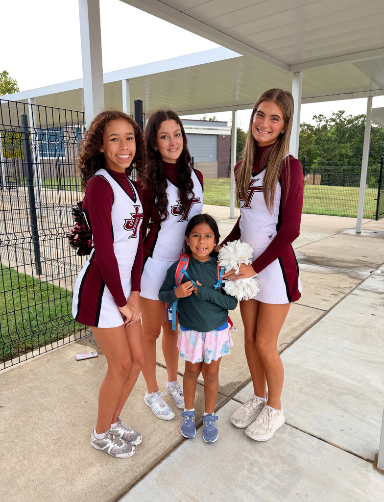 Three cheerleaders smiling with one young female student on sidewalk outside Northwest Elementary