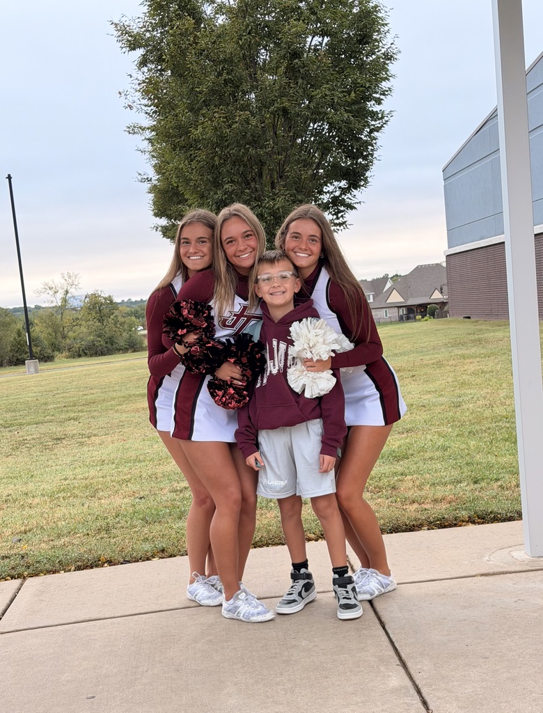 Three cheerleaders squeezing around student and smiling outside of Building F at West Elementary
