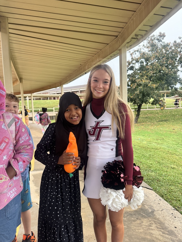 Cheerleader standing and smiling next to girl outside of East Elementary