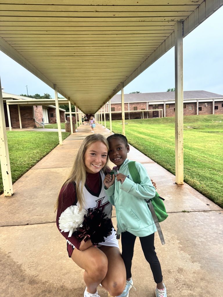 Cheerleader crouching down and smiling with early elementary student