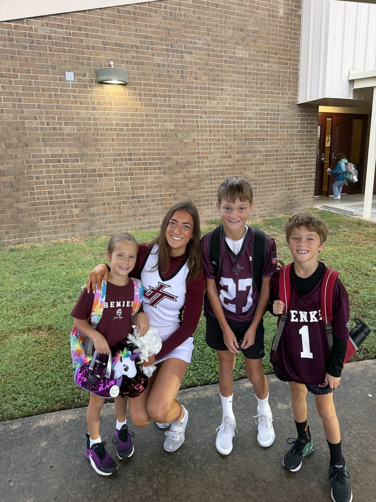Cheerleader kneeling down and smiling with three students by entrance to building at West Elementary