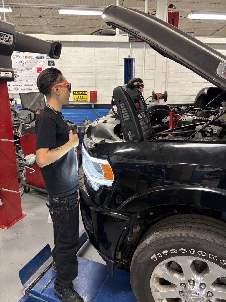 a student standing next to a car with its hood open