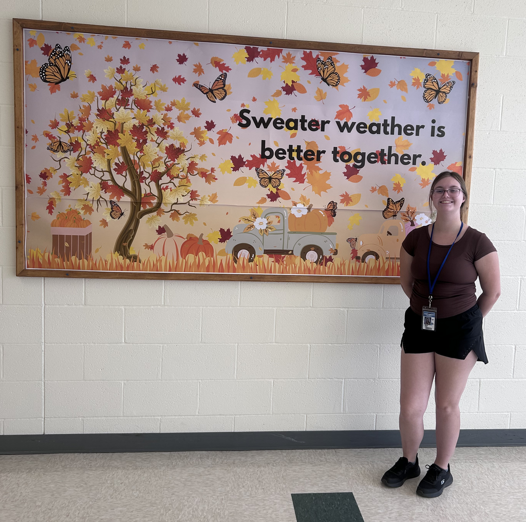 Fall bulletin board with student creator standing next to it.