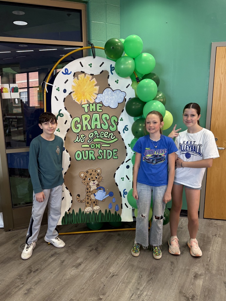 EJMS students standing in front of a banner with the 26-27 EJMS motto, "The grass is green on our side!"