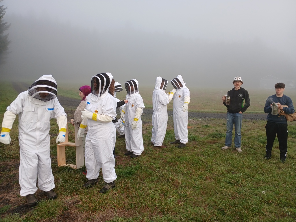 Students in white beekeeper suits checking beehive boxes.