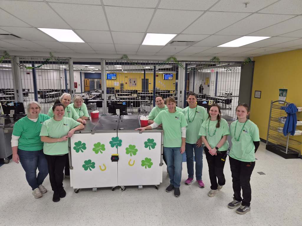 JHS lunch ladies and custodial staff posing together wearing green
