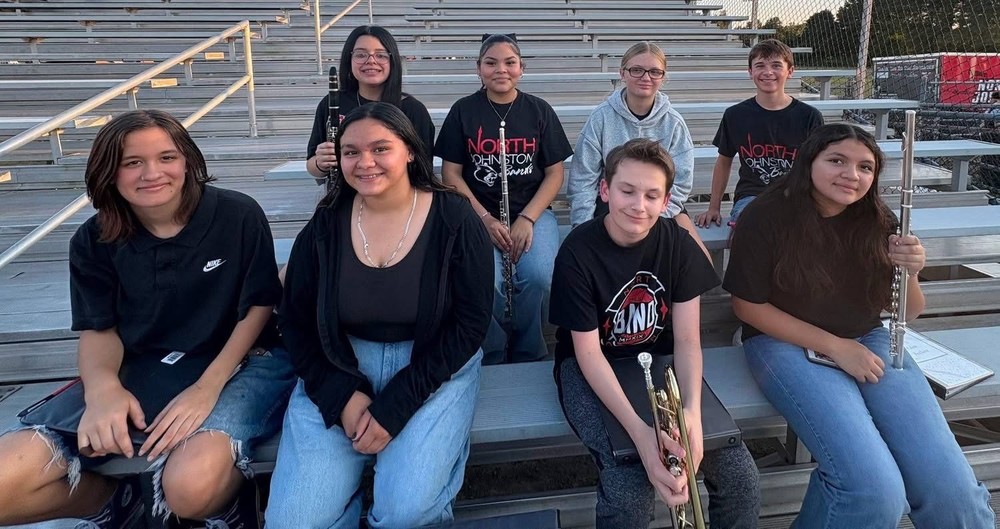 NJMS band students sitting on the bleachers holding their instruments 