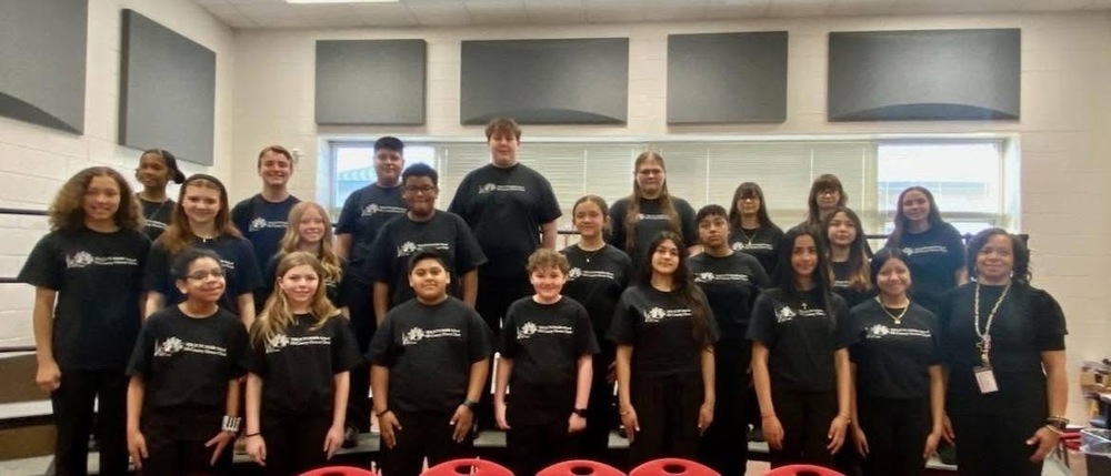 group chorus picture of students  in black shirts on the risers in the chorus room with the chorus director 