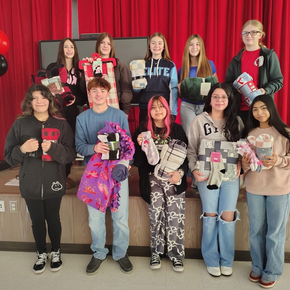 picture of students standing in front of a red curtain holding blankets and socks