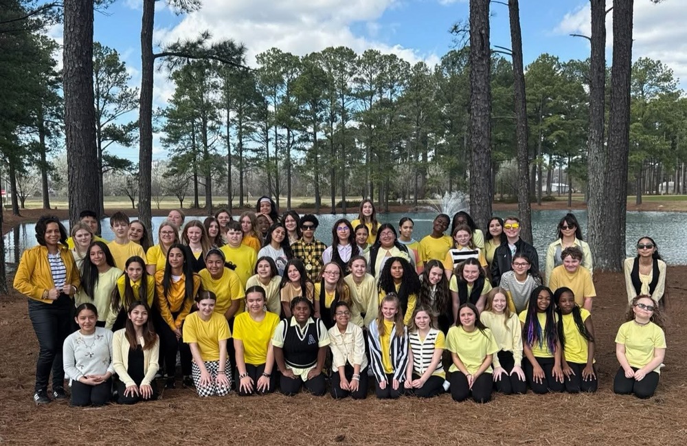 group of njms chorus students wearing yellow and black standing in front of trees and a pond 