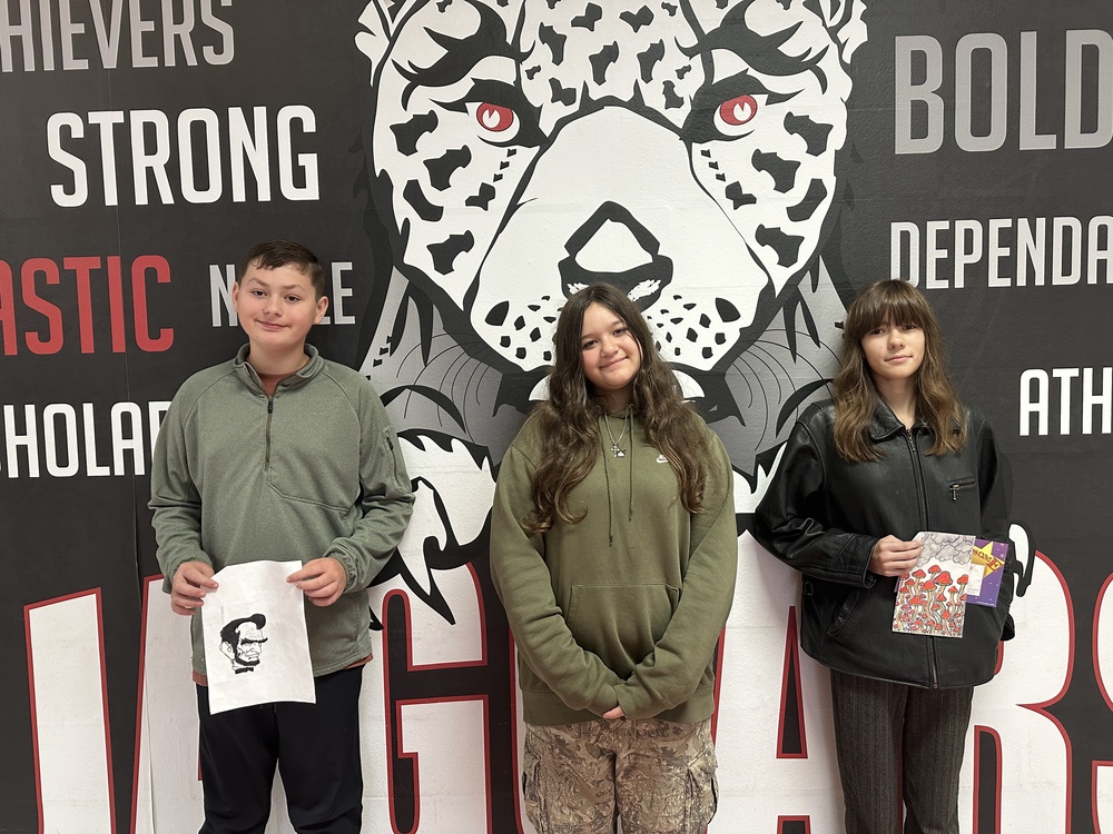 picture of 3 students holding up their art work and certificates in front of the jaguar mural