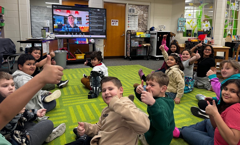 students seated in front of smartboard with zoom call in the background with author/illustrator Jeff Kinney
