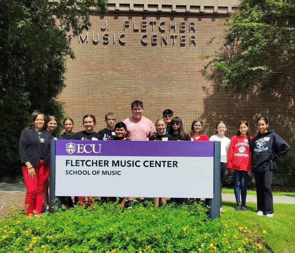 students and chorus director standing outside of fletcher music center on ECU's college campus