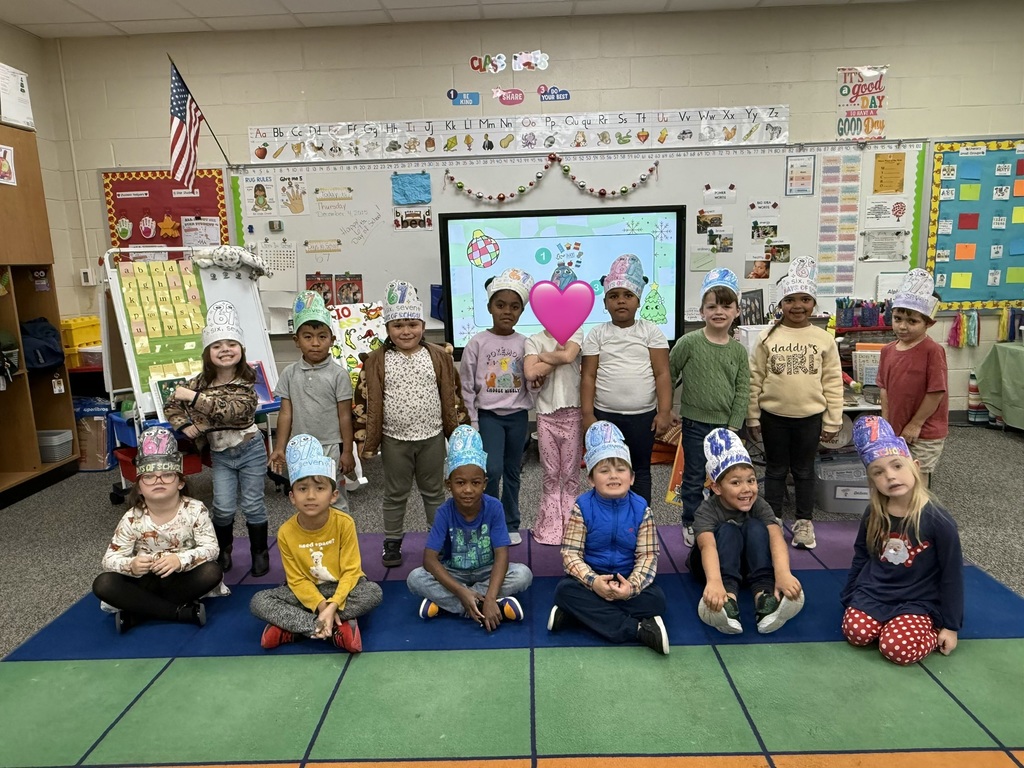 Group of kindergarten students  in front of smart board smiling with their 67 hats