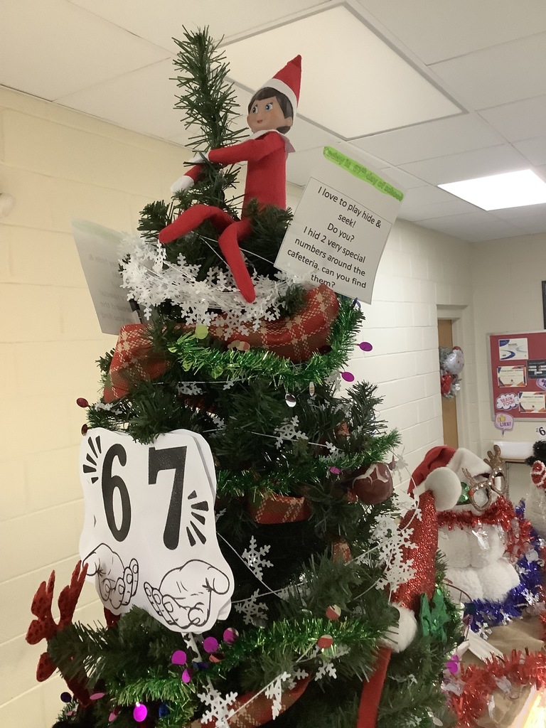 Cafeteria elf atop the cafeteria Christmas tree with 67 print out