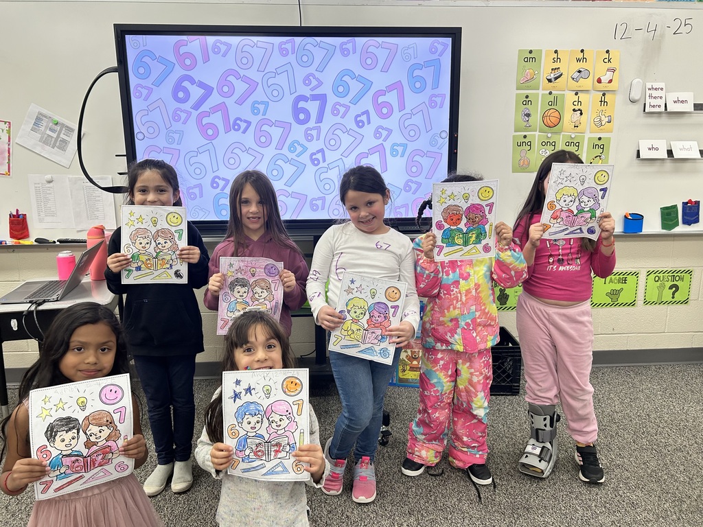 Group of first grader girls in front of smart board holding coloring page 