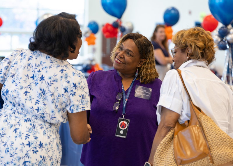 A lady in a purple shirt talks with two other ladies.