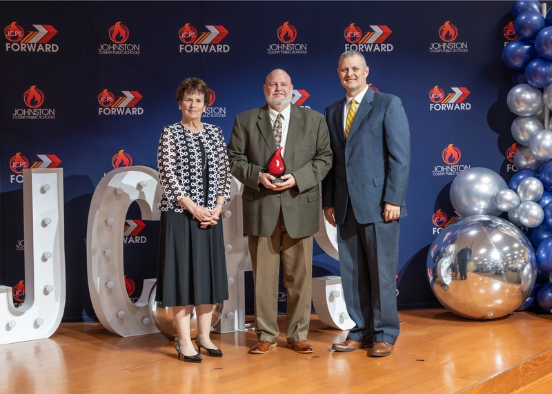 Dr. Todd Holmes (center) stands with Johnston County Board of Education Chair Lyn Andrews (left) and JCPS Superintendent Dr. David Pearce (right) after being presented with a Spotlight on Excellence Award as the 2026 Human Resources Employee of the Year.