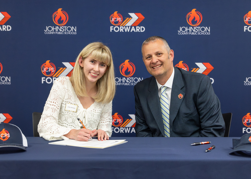 A contract signee smiles as she signs her contract beside Superintendent Dr. David Pearce