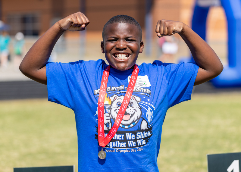 A West Clayton Elementary Special Olympics student flexes and flashes a big smile after receiving his medal after competing in the games.