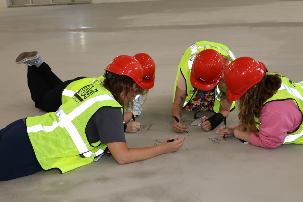 Four teachers sign their name on the floor