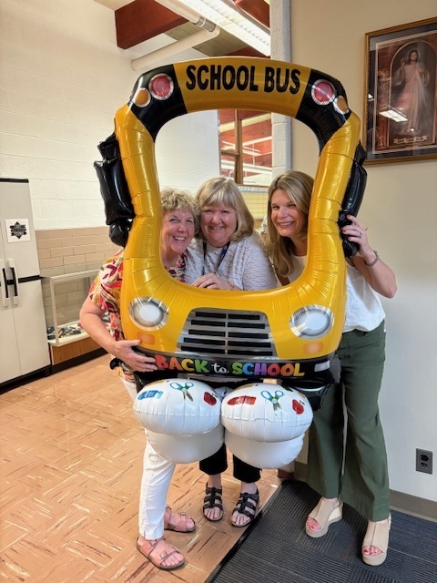 photo of three adults posing with a school bus balloon frame in a hallway