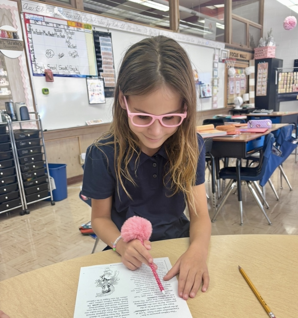 student using pink fluffy pen to follow along while reading a story.
