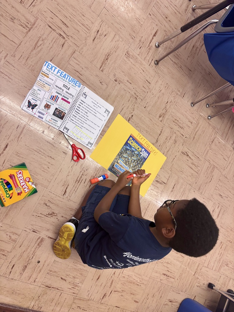 student sitting on classroom floor gluing photos on a poster