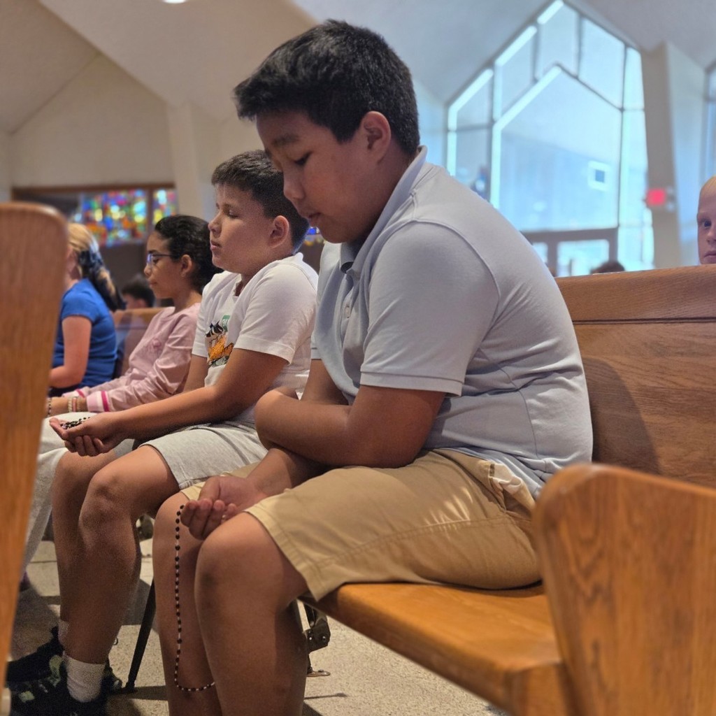 students sitting on pews praying the rosary
