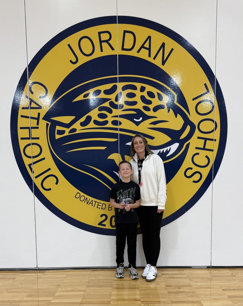 student posing with teacher in front of school logo on white wall