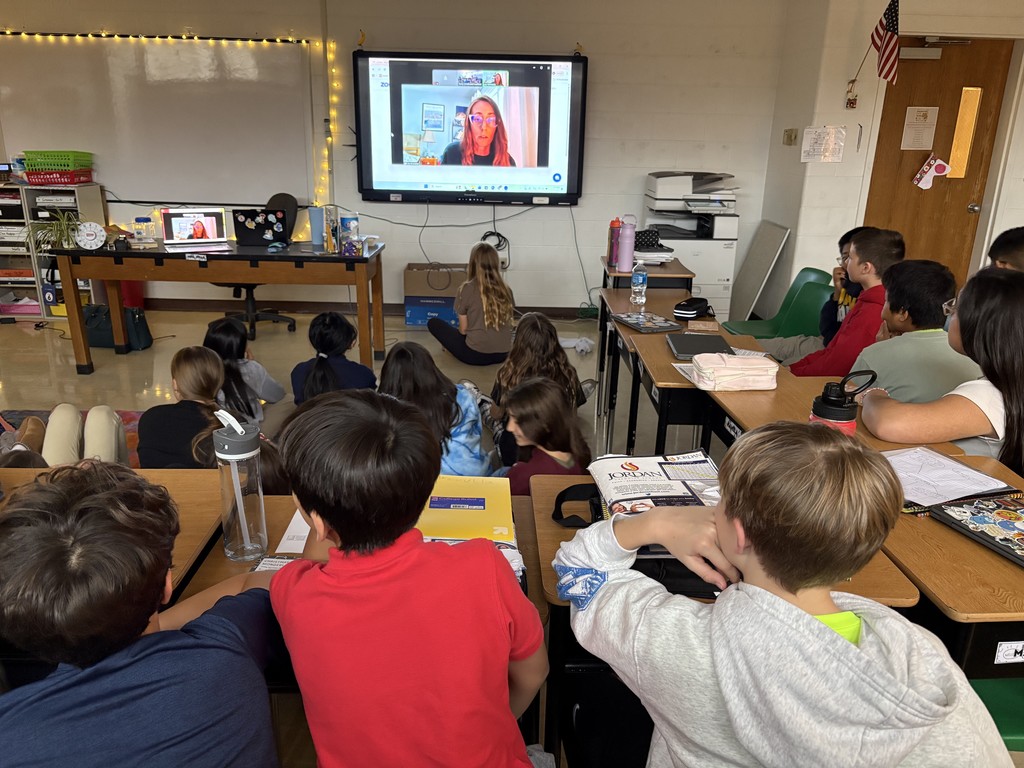 students seated at desks meeting with an author in a video call