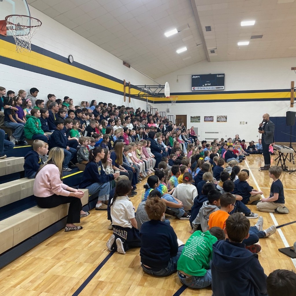 man speaking to group of students in a gym