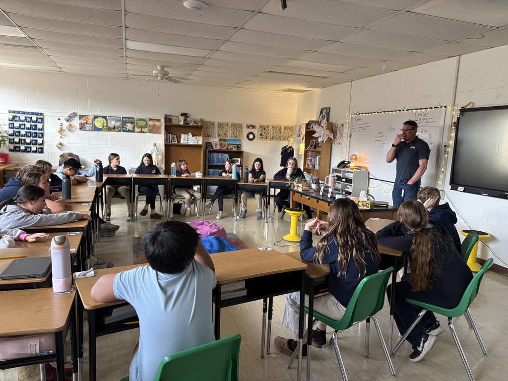 students seated at desks listening to guest speaker